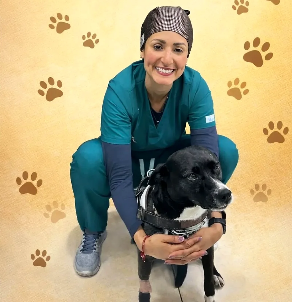 La Dra. Yoneidys Barrada agachada, sonriendo, abrazando a un perro negro con arnés